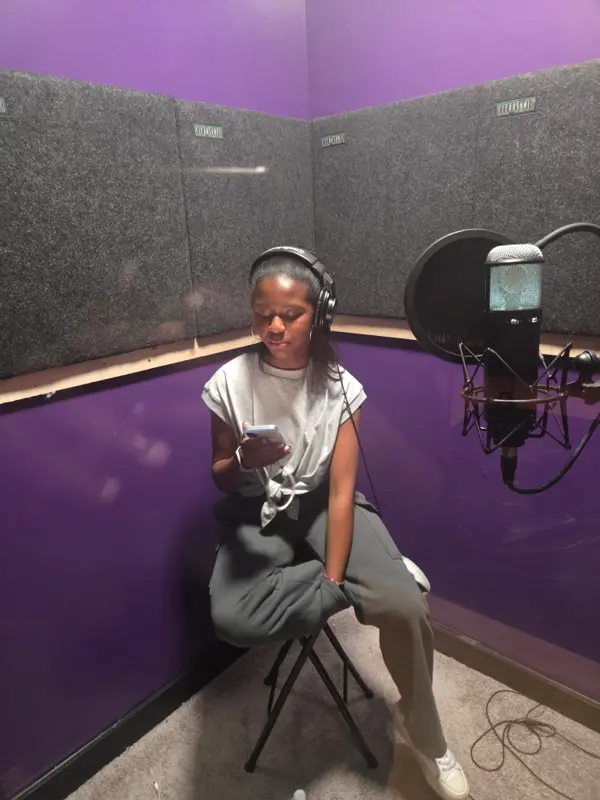 London Koi in headphones in a purple vocal booth, seated beside the studio microphone during a recording session